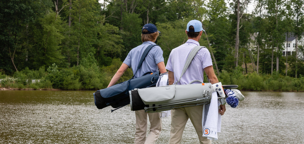 A picture of two golfers walking a course and carrying their Sunday Golf Bags on their shoulders.
